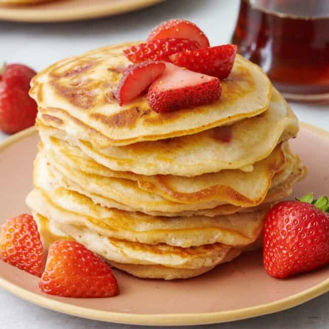 Stack of fresh strawberry pancakes on a plate with more fresh strawberries around.