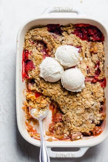 Final rhubarb crisp with scoop taken out and ice cream scoops on top of baking dish