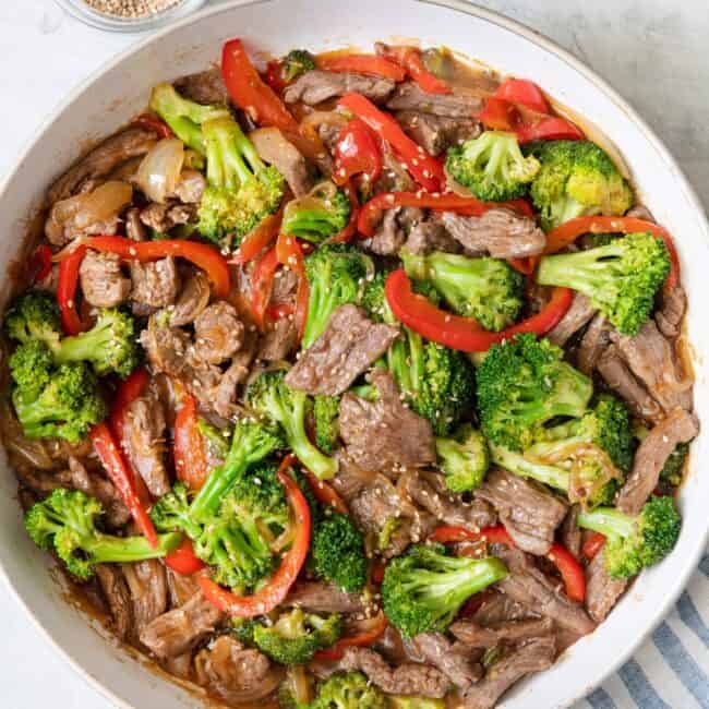 Overhead shot of teriyaki beef stir fry in a large skillet garnished with sesame seeds.