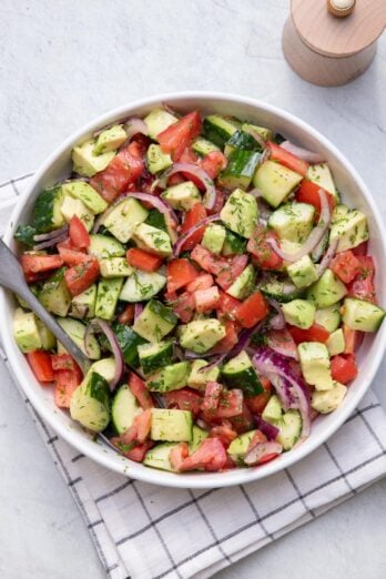 Big white bowl of Tomato Avocado Cucumber Salad all mixed up with a spoon in the large bowl.