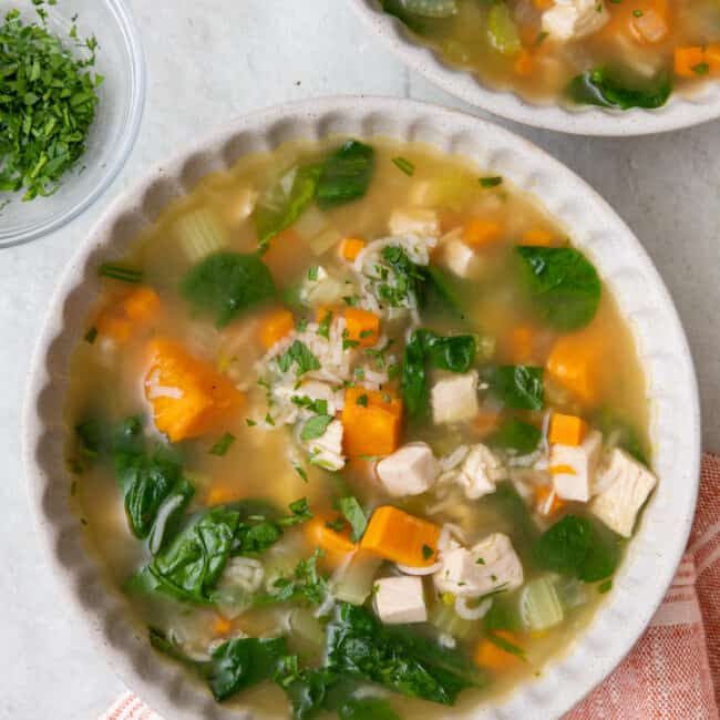 A bowl of leftover turkey and rice soup with another bowl nearby.