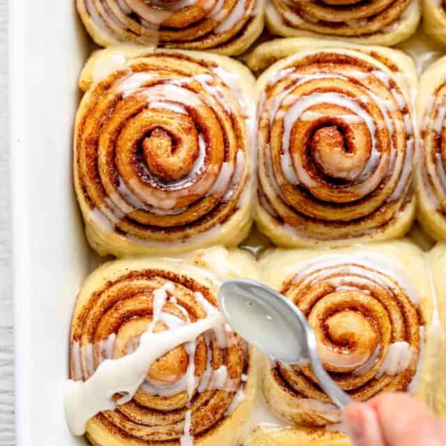 Spoon glazing vegan cinnamon rolls in white pan