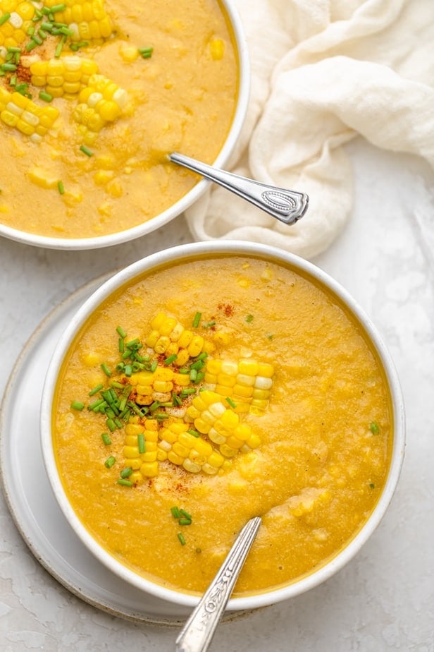 Two bowls of vegan corn chowder with spoons inside