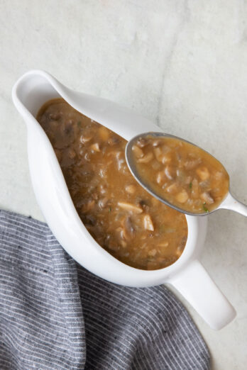 White gravy boat with the final vegan mushroom gravy and a spoon scooping some out.