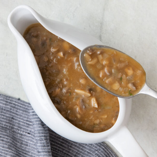 White gravy boat with the final vegan mushroom gravy and a spoon scooping some out.