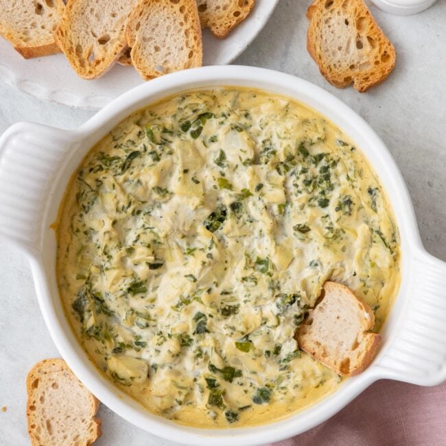 Overhead image of spinach artichoke dip after baked being served with a plate of toasted crostinis for dipping with one inside dip.