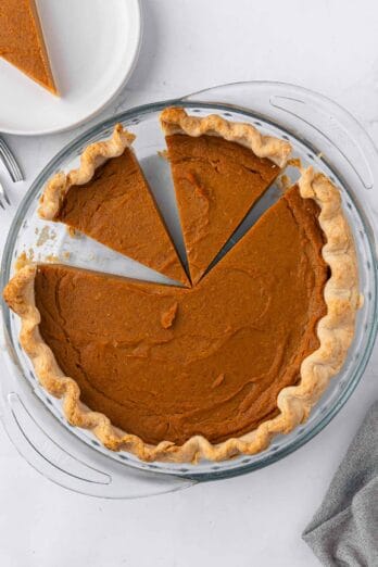 Vegan sweet potato pie in glass pie dish with a few slices cut.