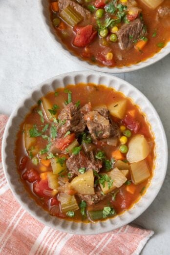 Two bowls of chunky veggie soup garnished with parsley with one bowl in focus.