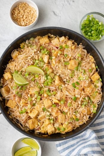 Vegetarian pad thai with tofu garnished with green onions and lemon wedges.