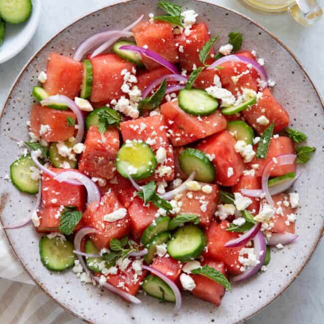 Watermelon feta salad served in a large bowl with cucumbers and onions.