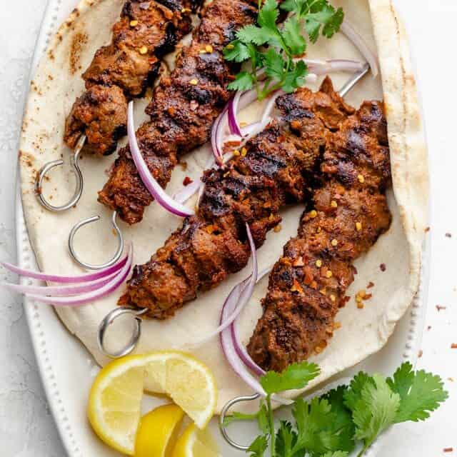 Large plate of the West African Beef Kabobs served on top of pita with lemon slices and herbs