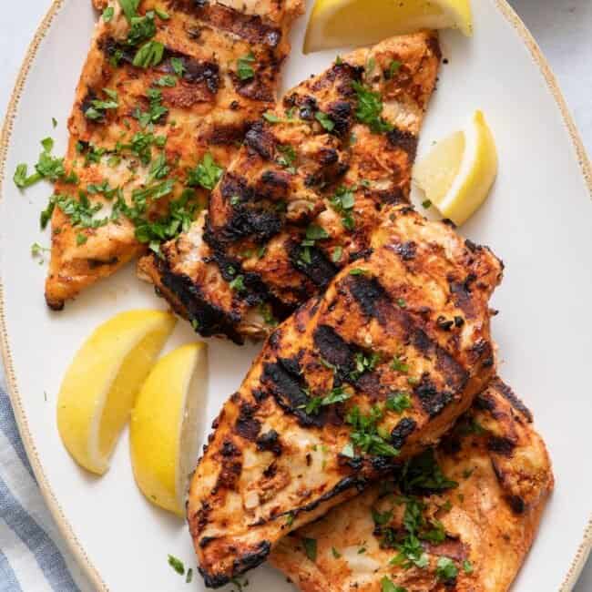 Over head shot showing 4 grilled chicken breasts on plate garnished with lemon wedges and parsley.