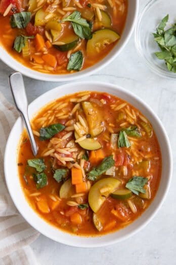 2 bowls of soup with spoon and fresh torn basil.