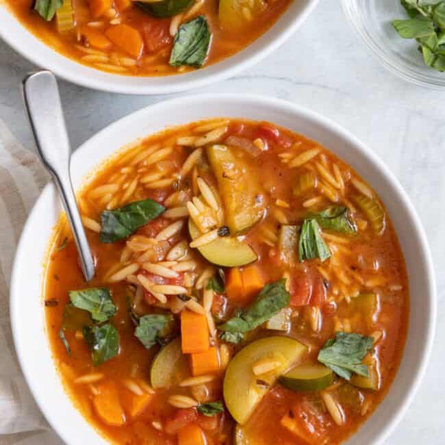 2 bowls of soup with spoon and fresh torn basil.