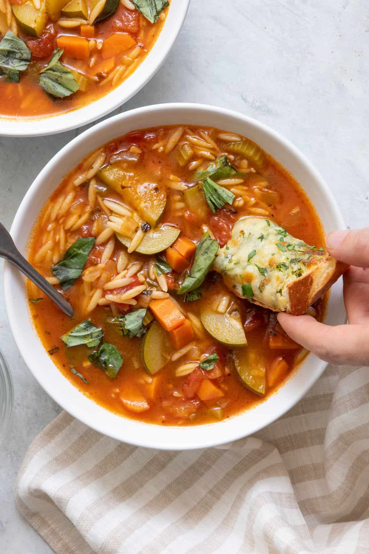 Hand dipping a piece of cheese bread into soup.