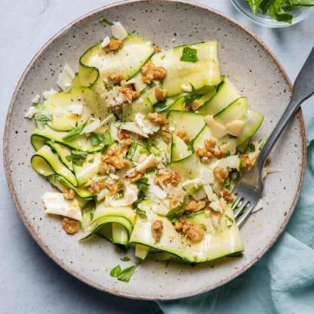 Large bowl of zucchini salad made with zucchini ribbons with blue towel and serving ware in bowl